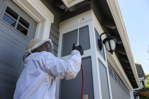Stop Bugging Me's extermination technician applies treatment by a garage to fight wasps, hornets, and yellow jackets.